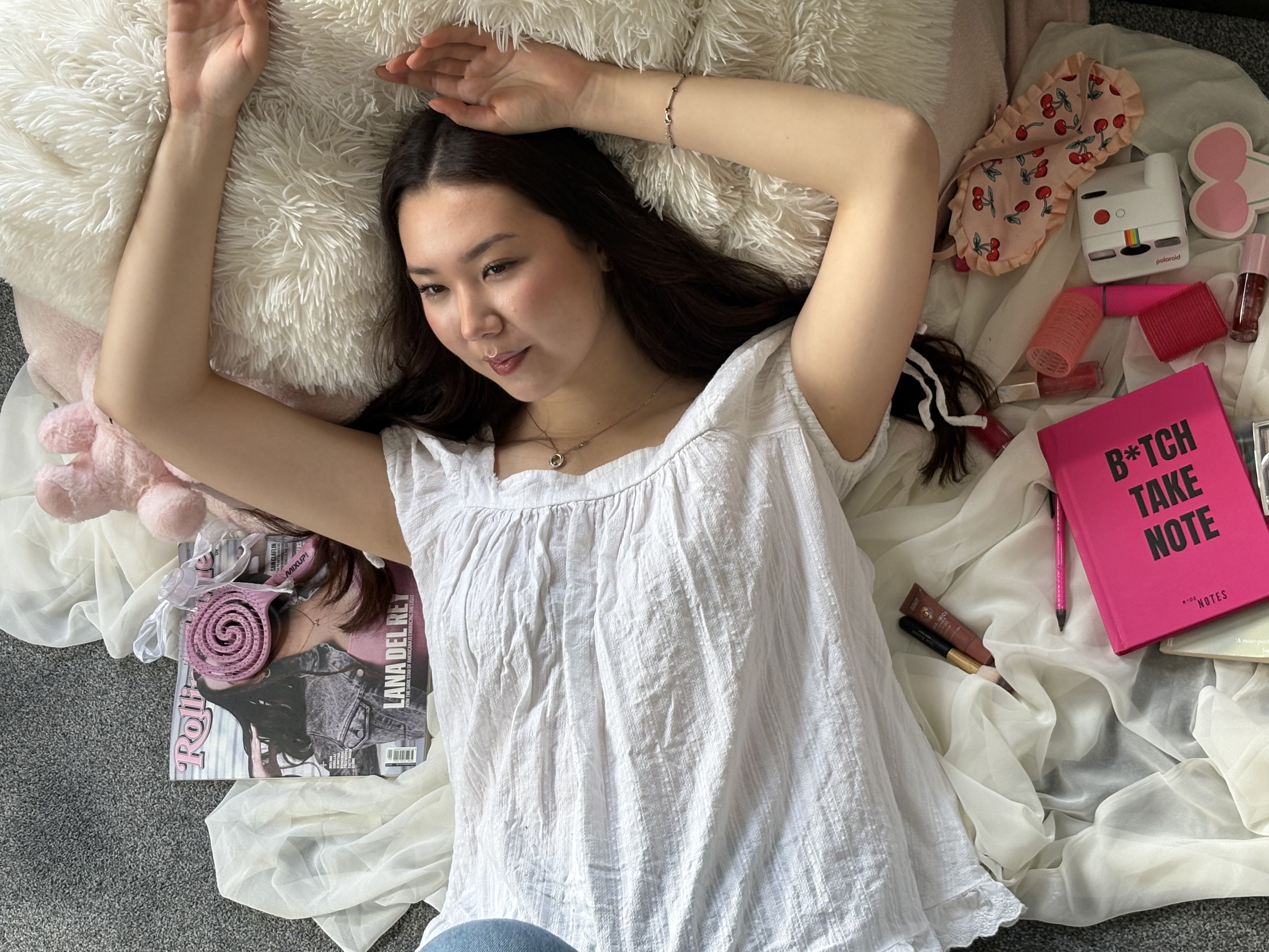 Pink girl on white bedding, arms up, B*TCH TAKE NOTE notebook beside her